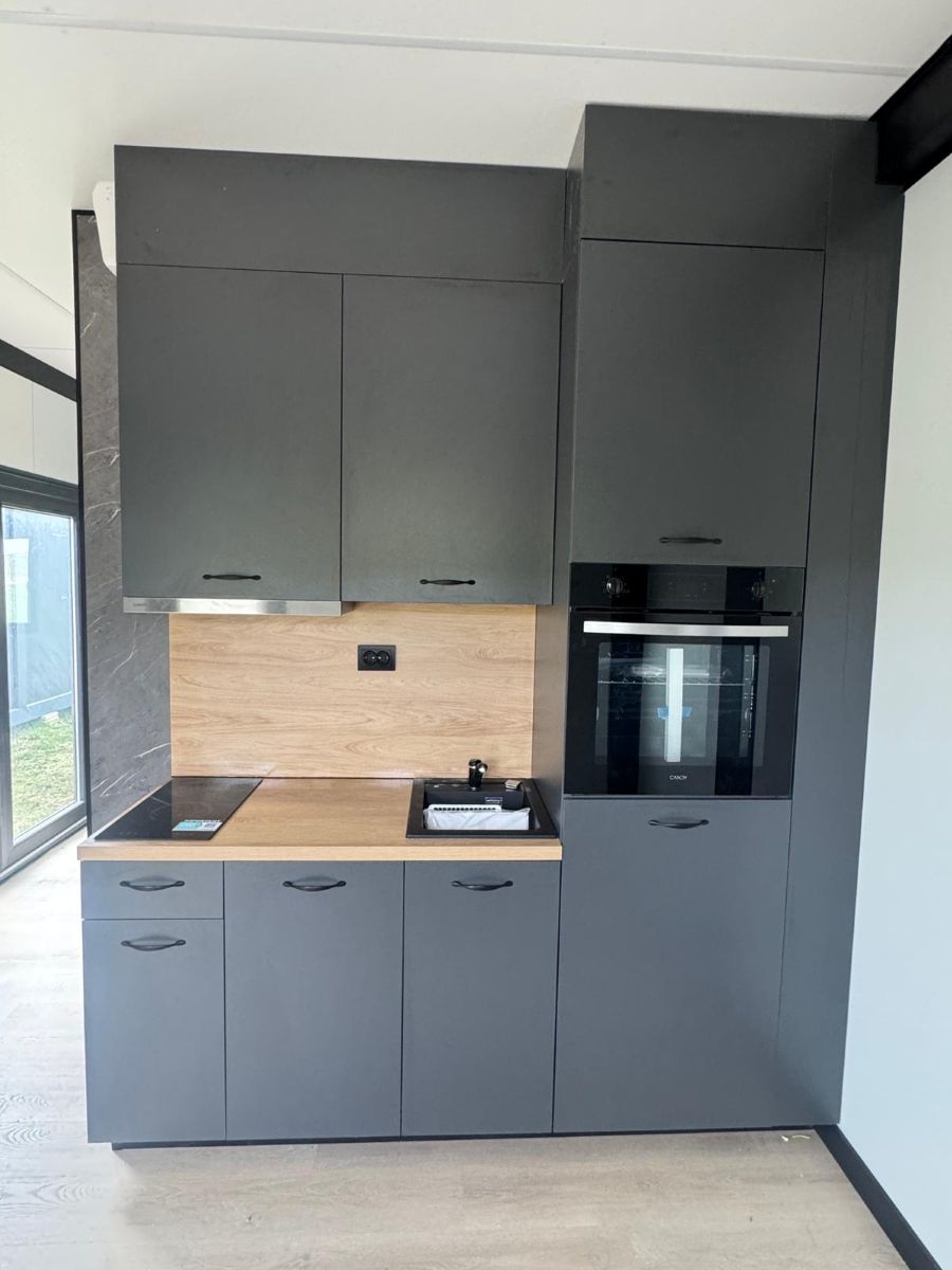 Compacte keuken in mantelzorgwoning met grijze kasten en houten backsplash