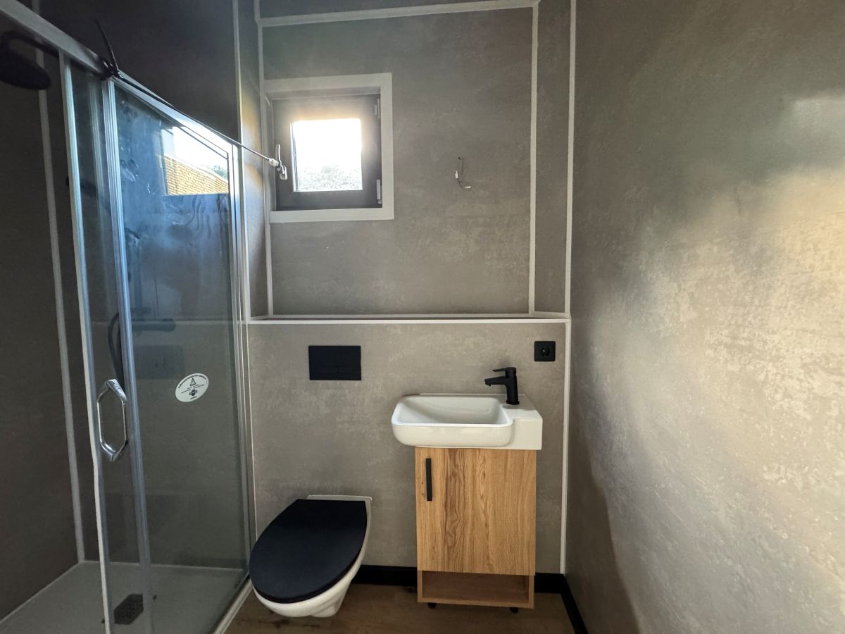 Volledige badkamer in noodwoning met inloopdouche, fonteintje en zwart toilet